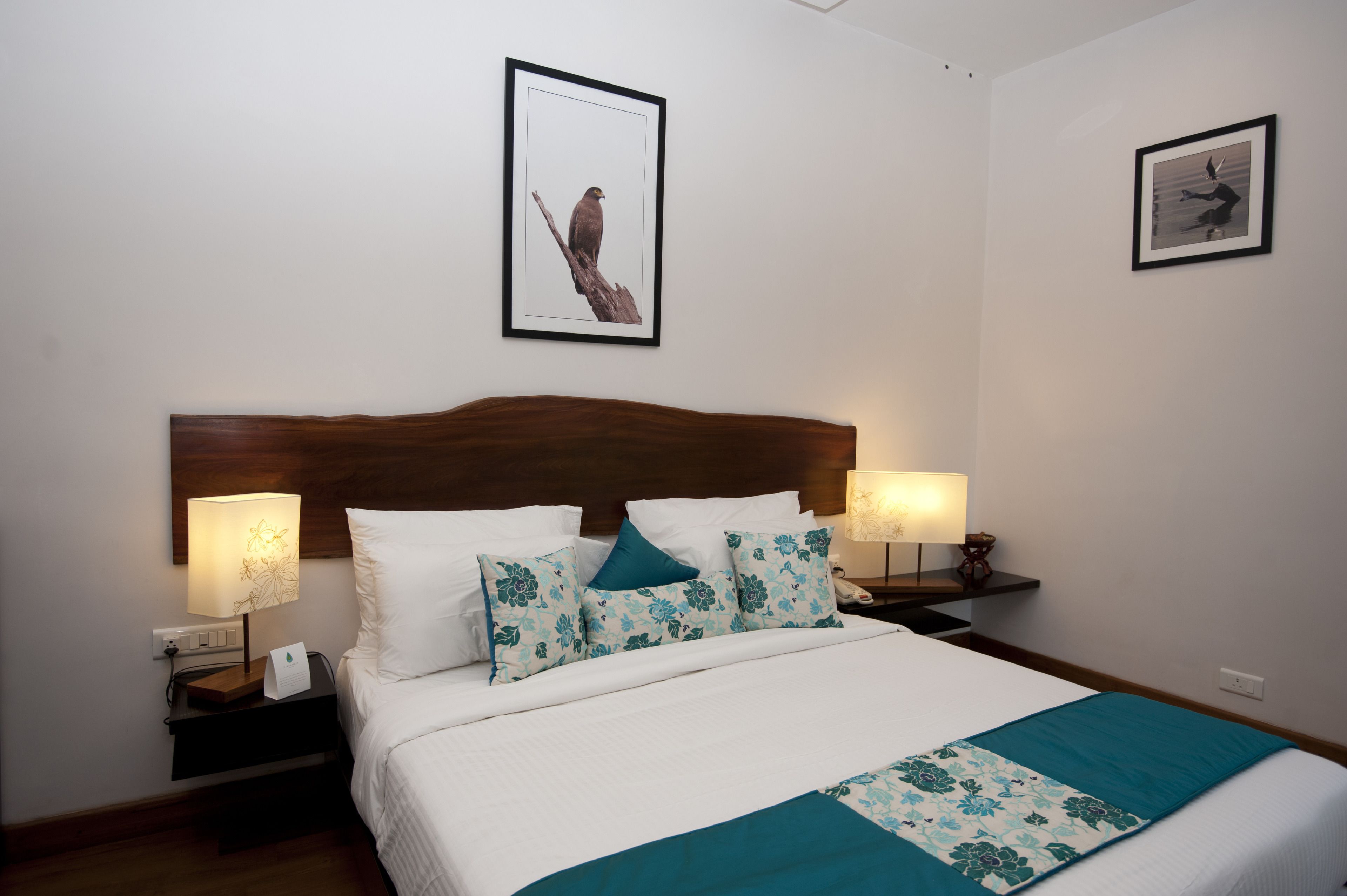 A neatly made bed with floral pillows, two bedside lamps, and framed pictures on the wall.