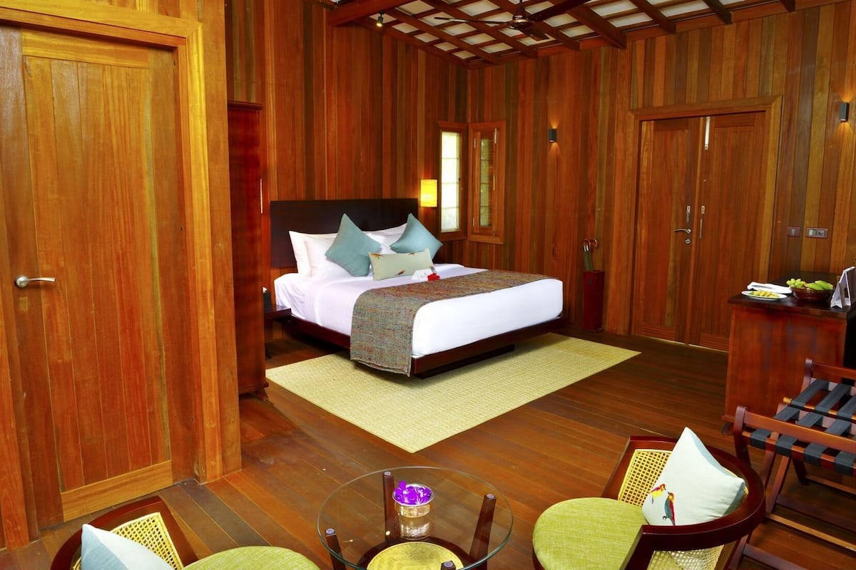 A wooden-themed room with a bed, a glass table, and chairs.