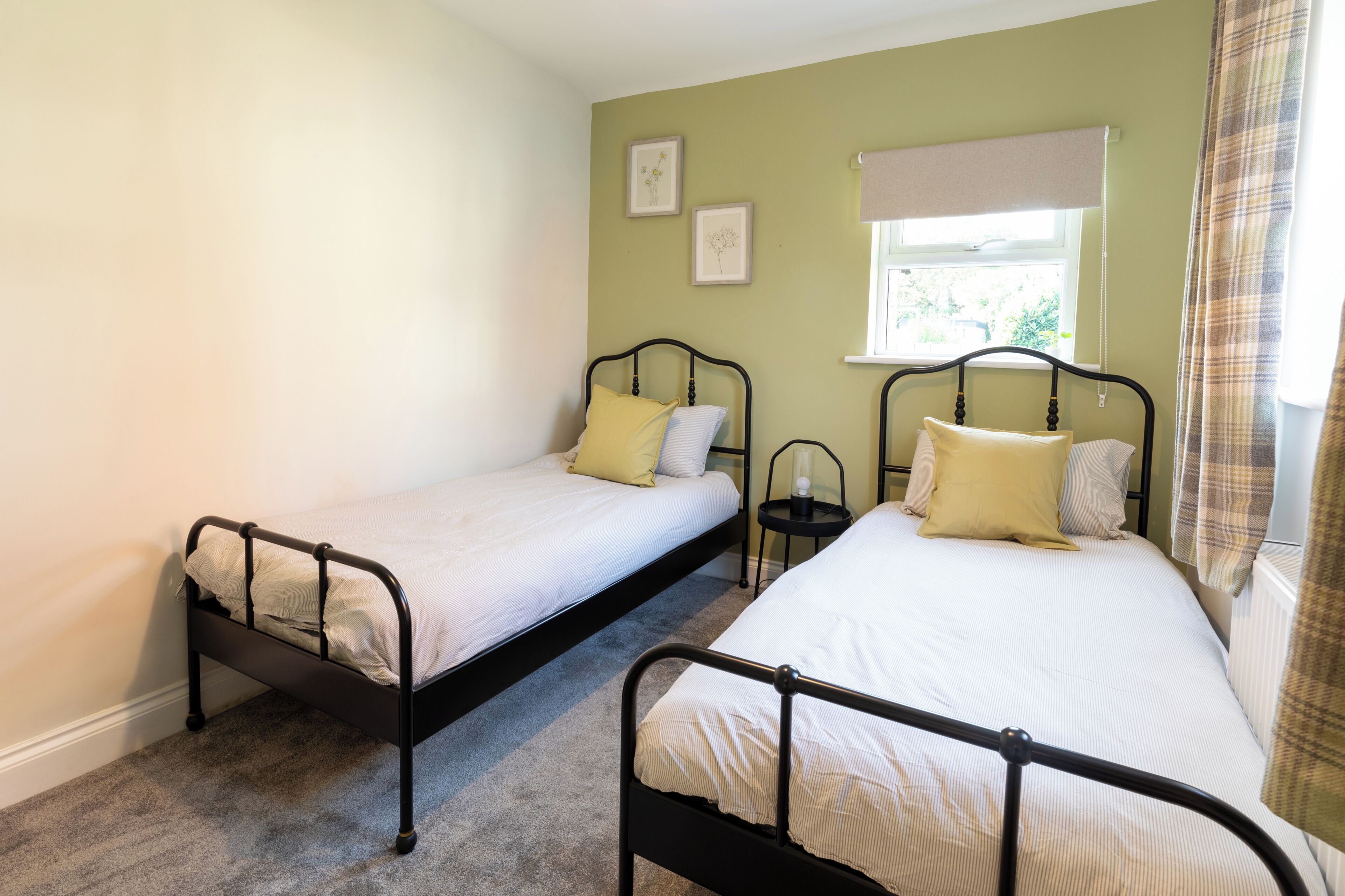 A room with two single beds, a small bedside table with a lamp, and a window with a blind.