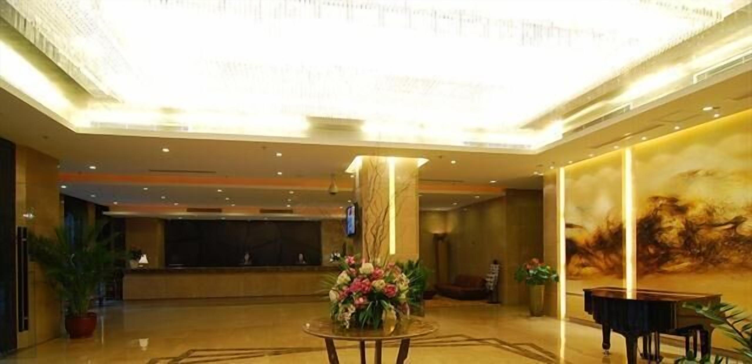 A spacious lobby with a high ceiling, a reception desk, a piano, and a floral arrangement.