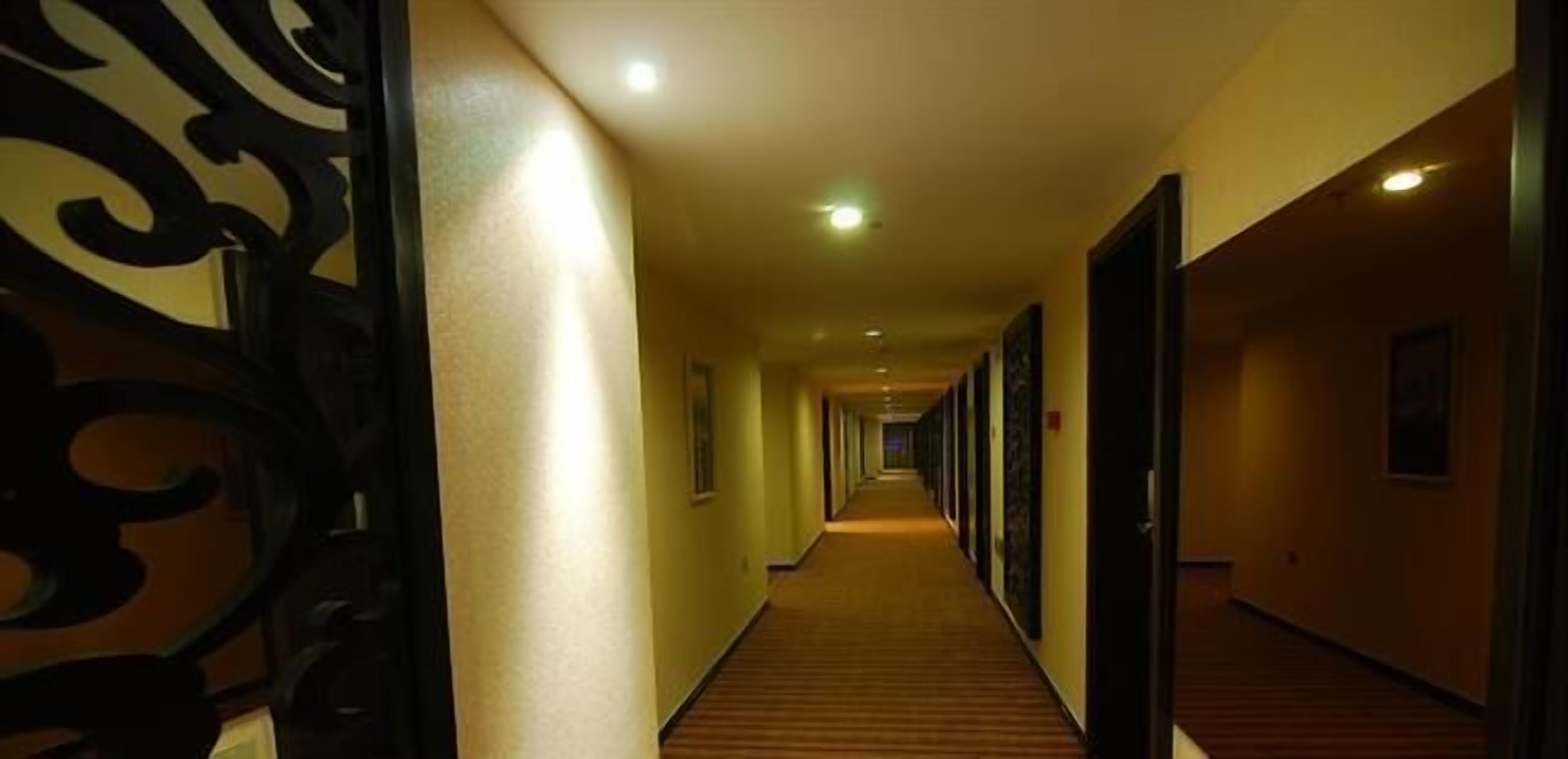 A long, narrow hotel corridor with wooden flooring and decorative black metal railings on the left.
