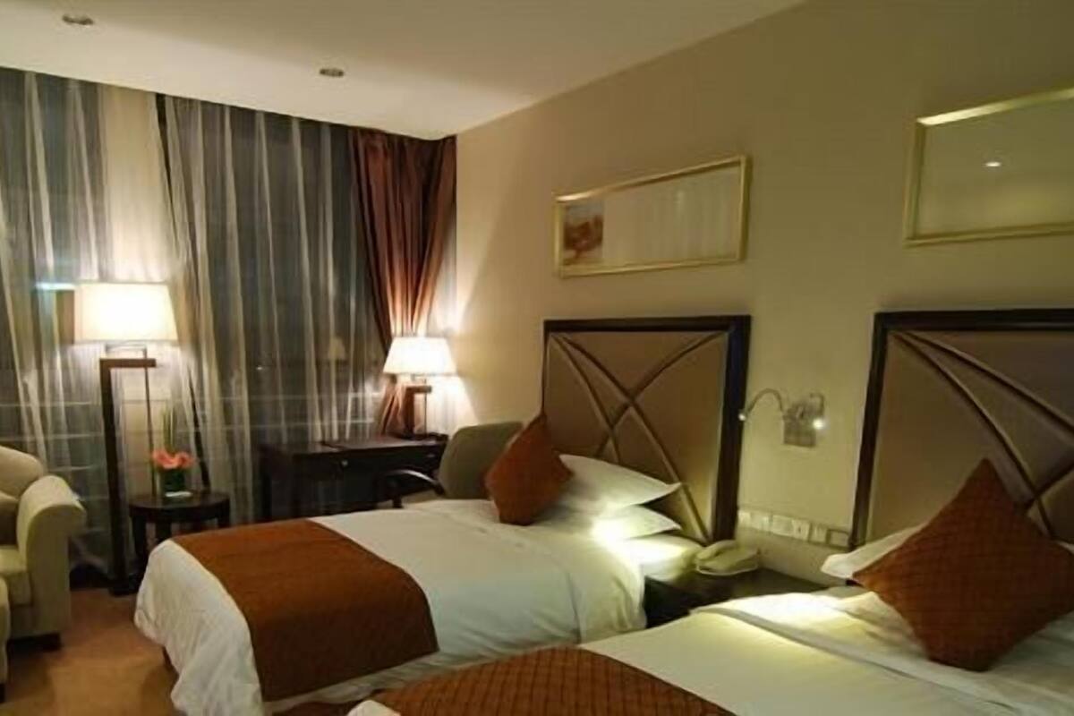A hotel room with two beds, a desk, a chair, and a large window with curtains.