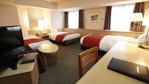 Habitación de hotel con tres camas, un escritorio, una silla, un televisor y una lámpara.