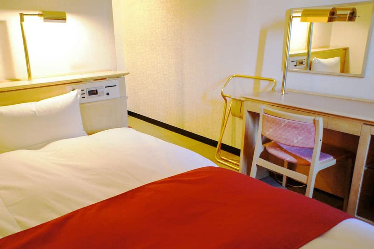 Hotellihuone, jossa on sänky, yöpöytä ja peili.