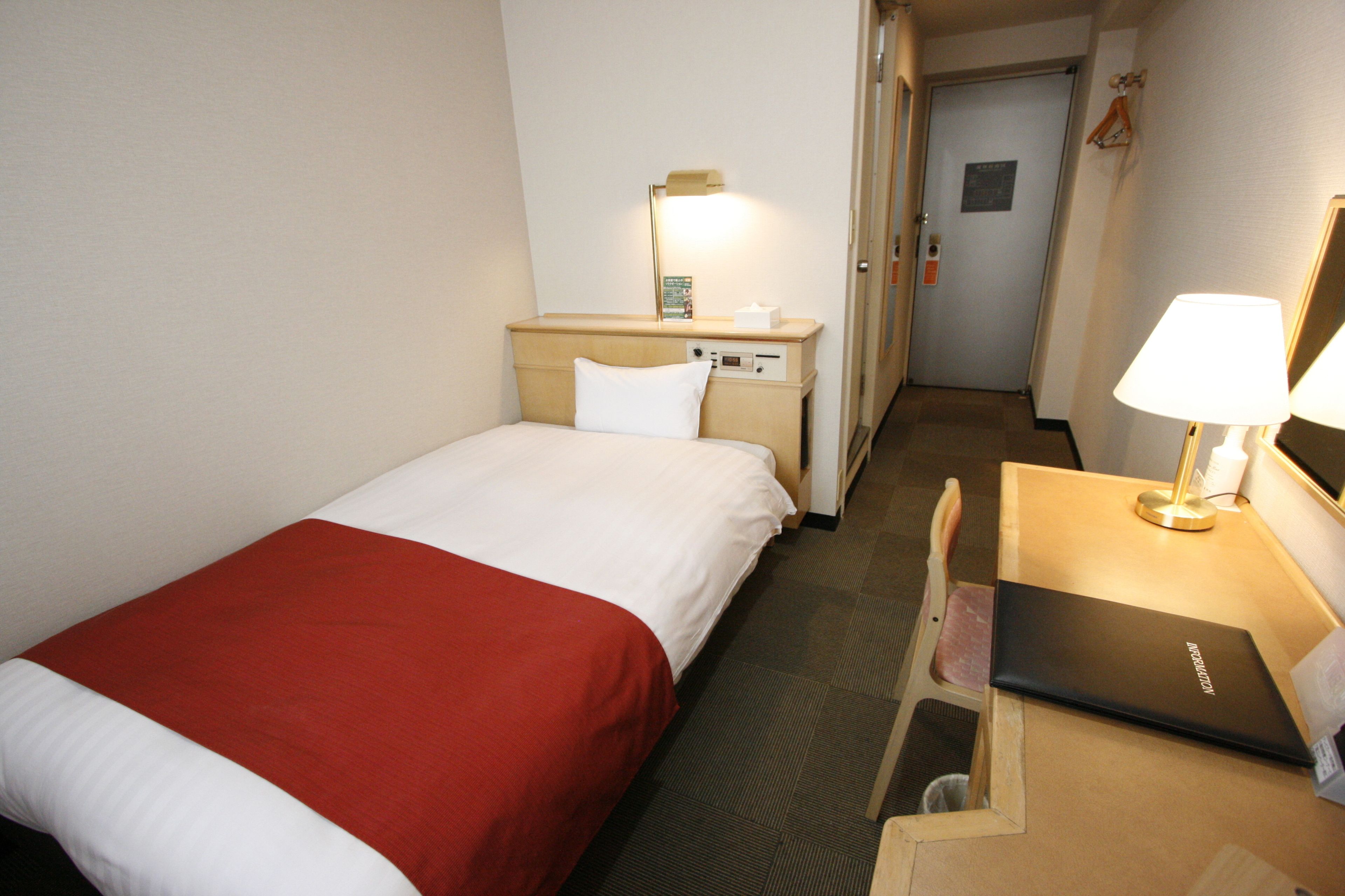 A hotel room with a bed, a desk, a lamp, and a nightstand with a lamp.