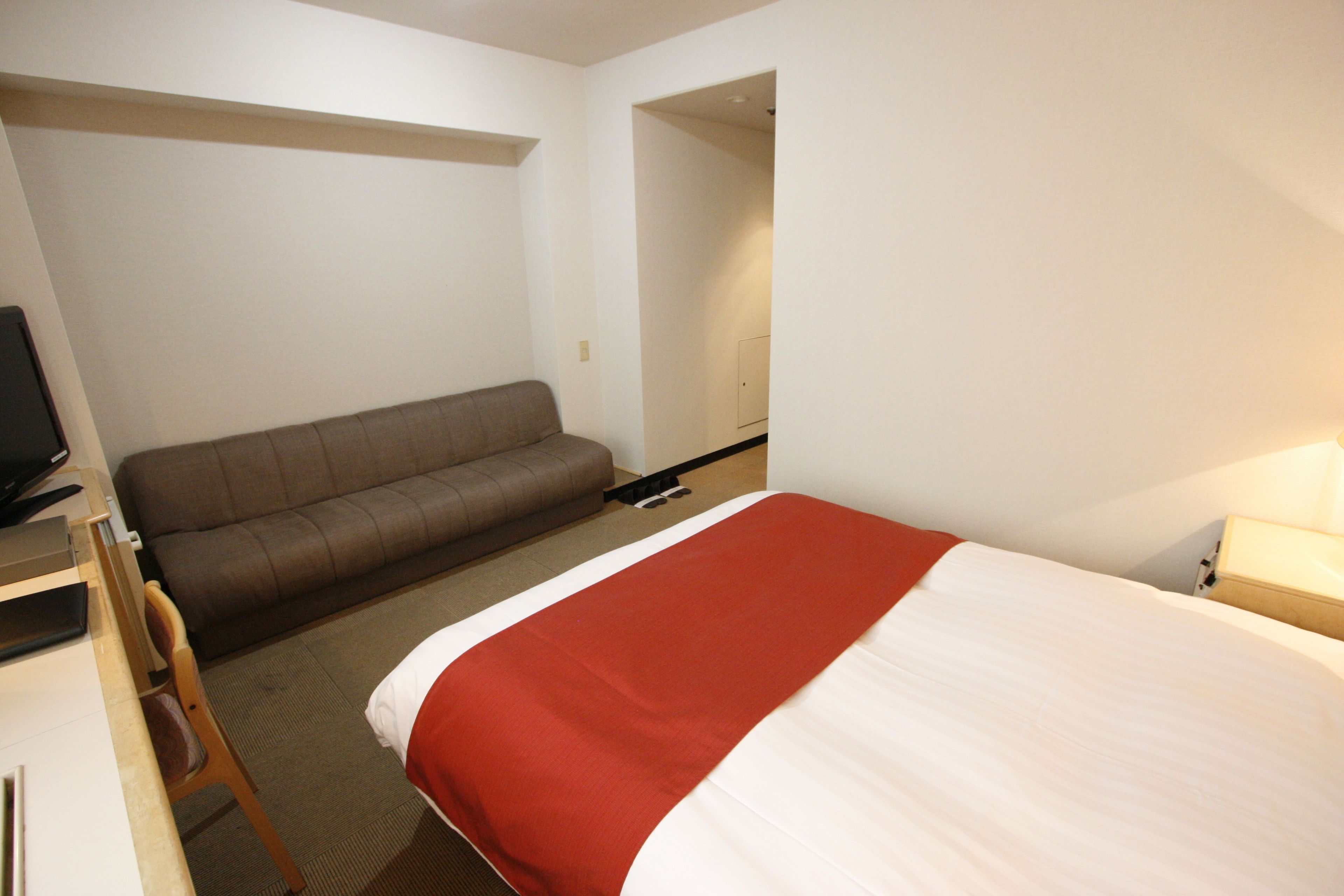 A hotel room with a bed, a sofa, a desk, and a television.