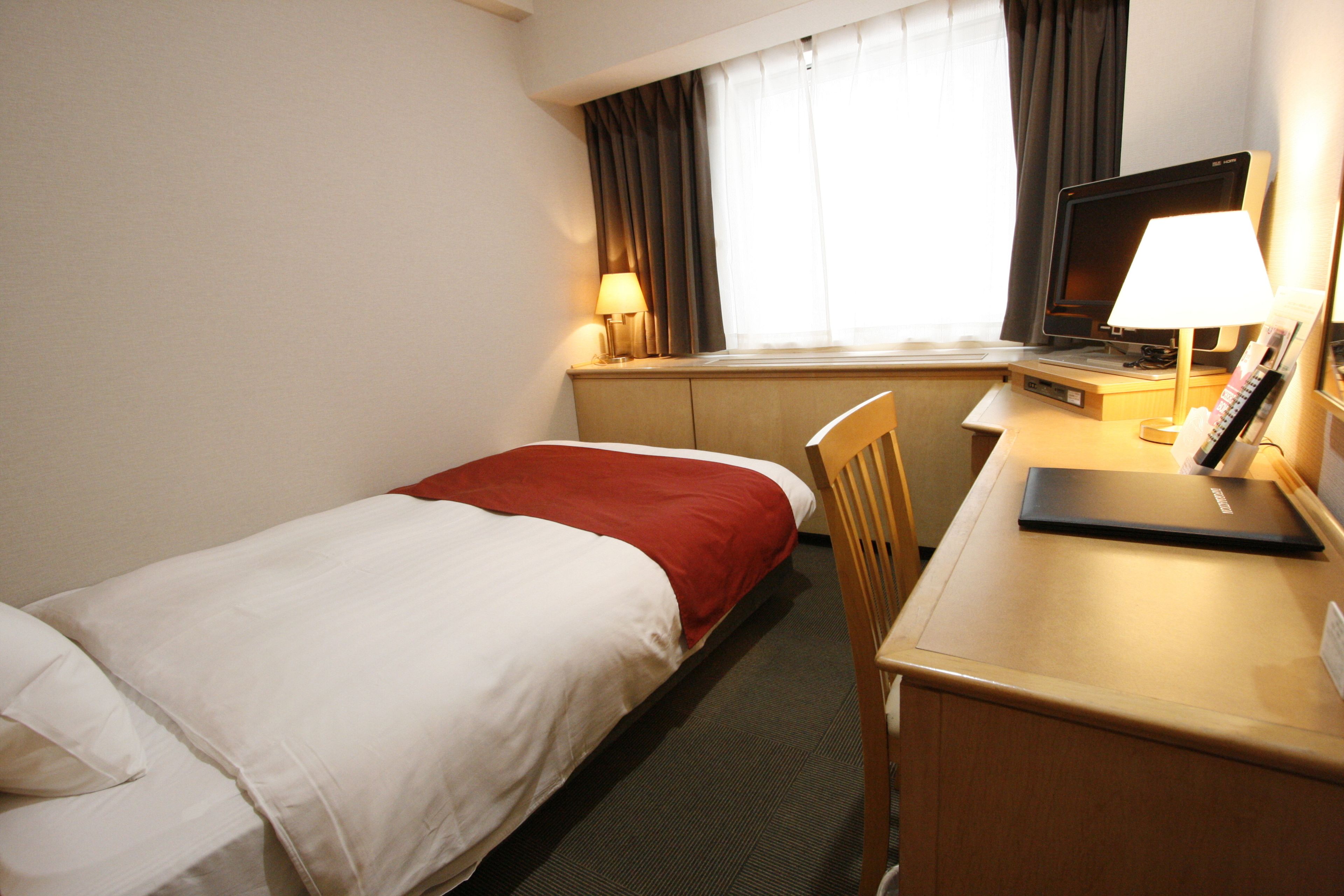 A hotel room with two beds, a desk with a laptop, a chair, a lamp, and a window with curtains.