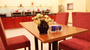 Comedor con mesa de madera, sillas tapizadas en rojo y un jarrón de flores blancas.
