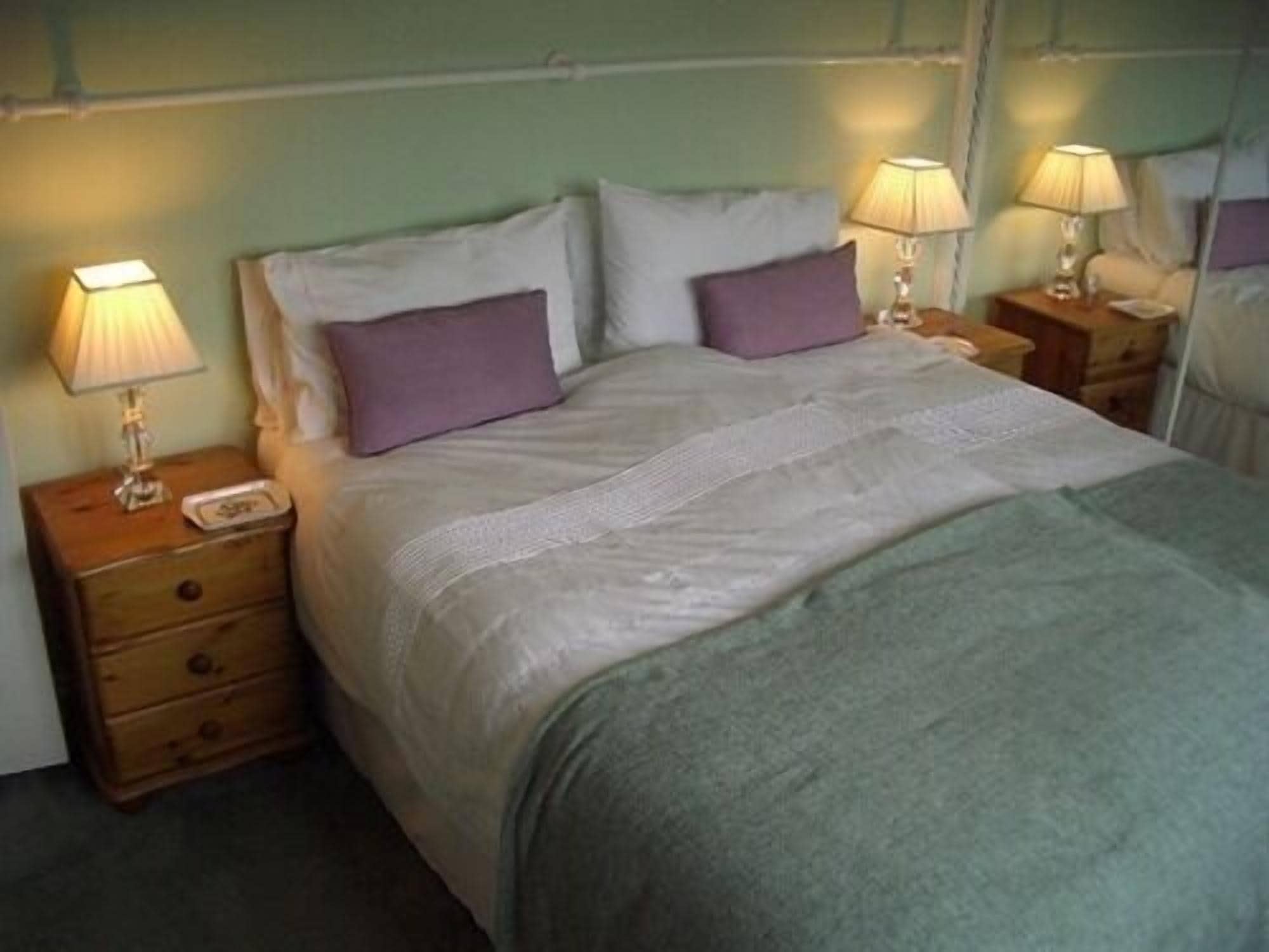 A neatly made bed with a white comforter and two purple pillows, flanked by wooden nightstands with lamps.