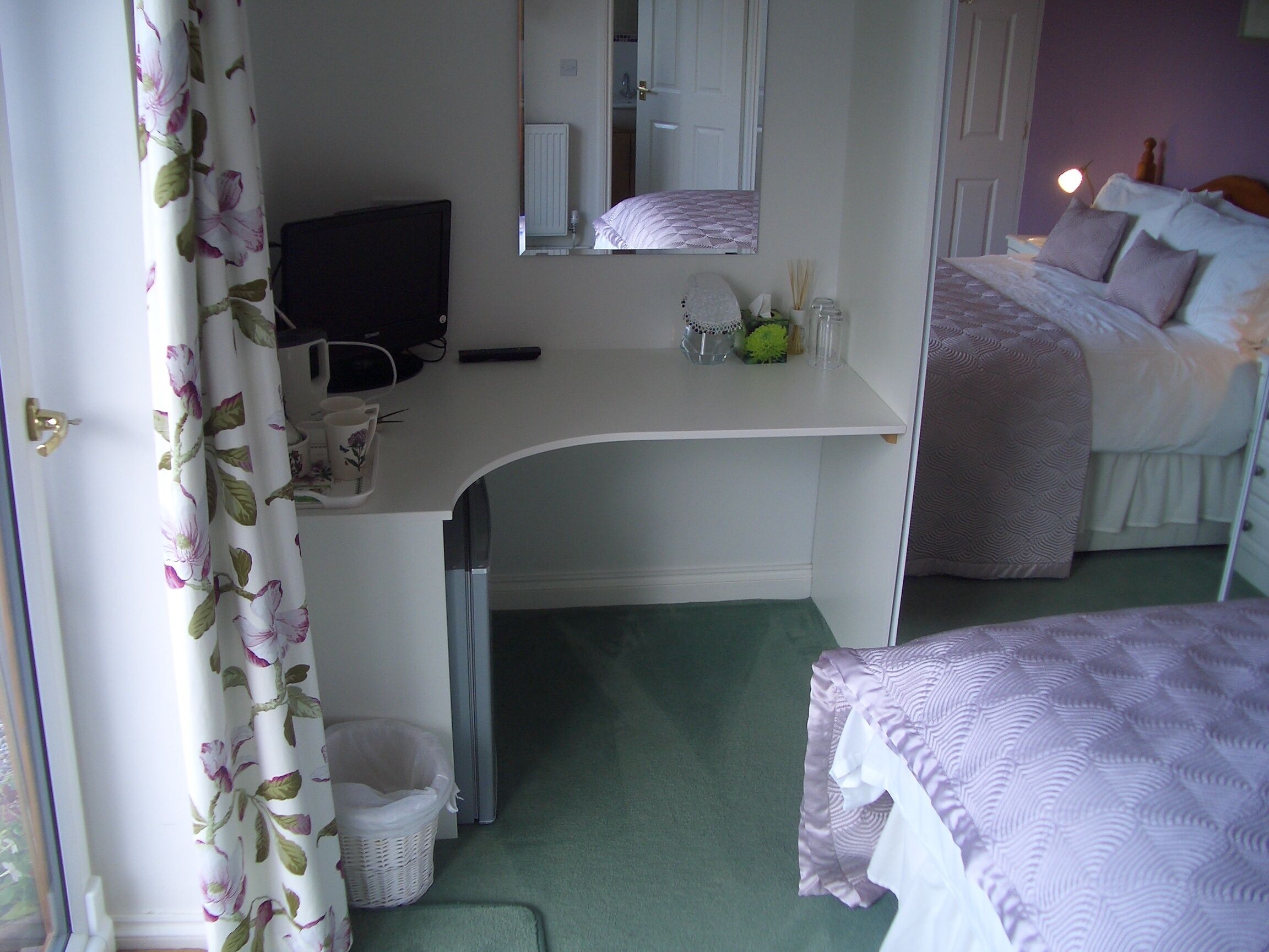 A bedroom with a desk, a bed, and a mirror.