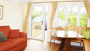A room with a wooden floor, a red sofa, a dining table with chairs, and a sliding glass door leading to a balcony. - Quixhill - Denstone - Dove Meadow B & B (Uttoxeter)