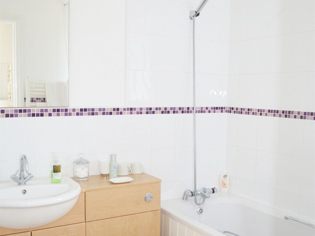 Un baño con lavamanos blanco, tocador de madera y bañera.