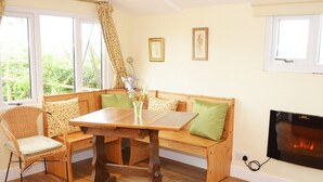 A cozy living room with a wooden table, wicker chair, and bench with green cushions. There is a fireplace and framed pictures on the wall. - Quixhill - Denstone - Dove Meadow B & B (Uttoxeter)