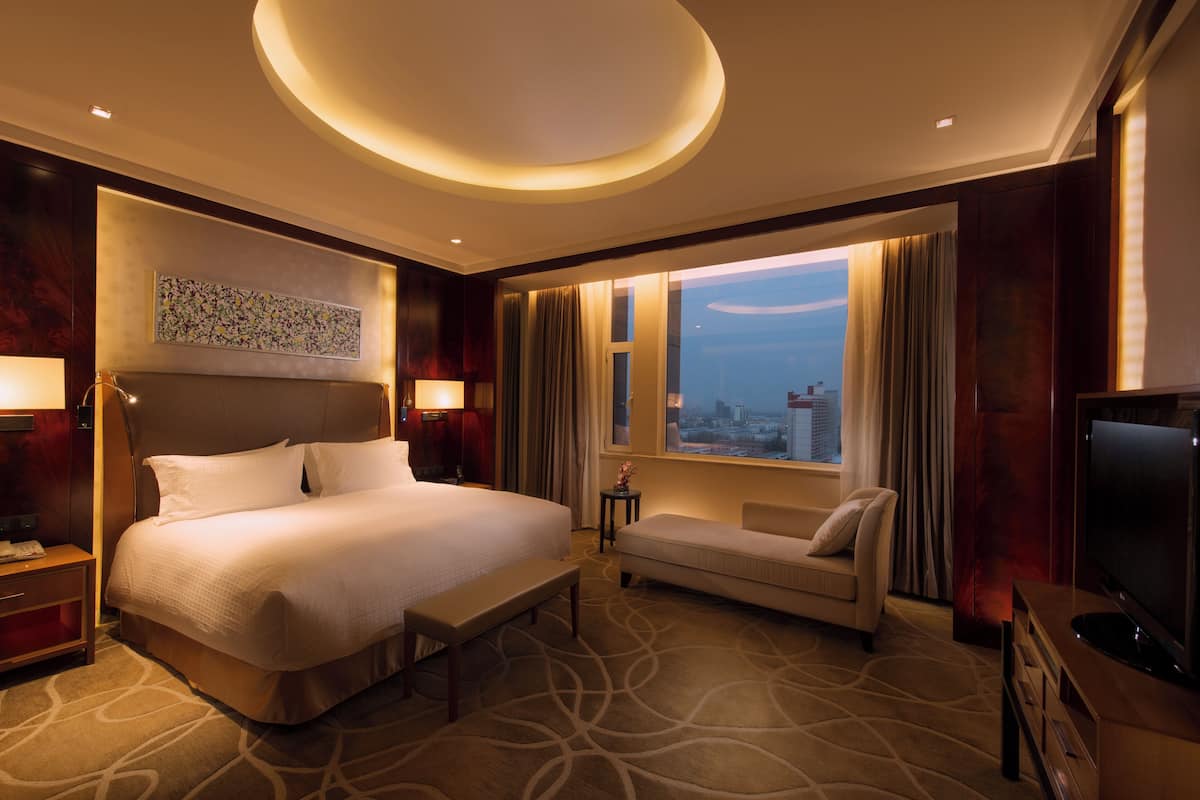 A hotel room with a large bed, a sofa, a TV, and a window with curtains.