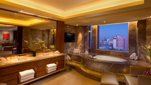 Un baño moderno con un espejo grande, una bañera y vistas de la ciudad a través de un ventanal amplio.