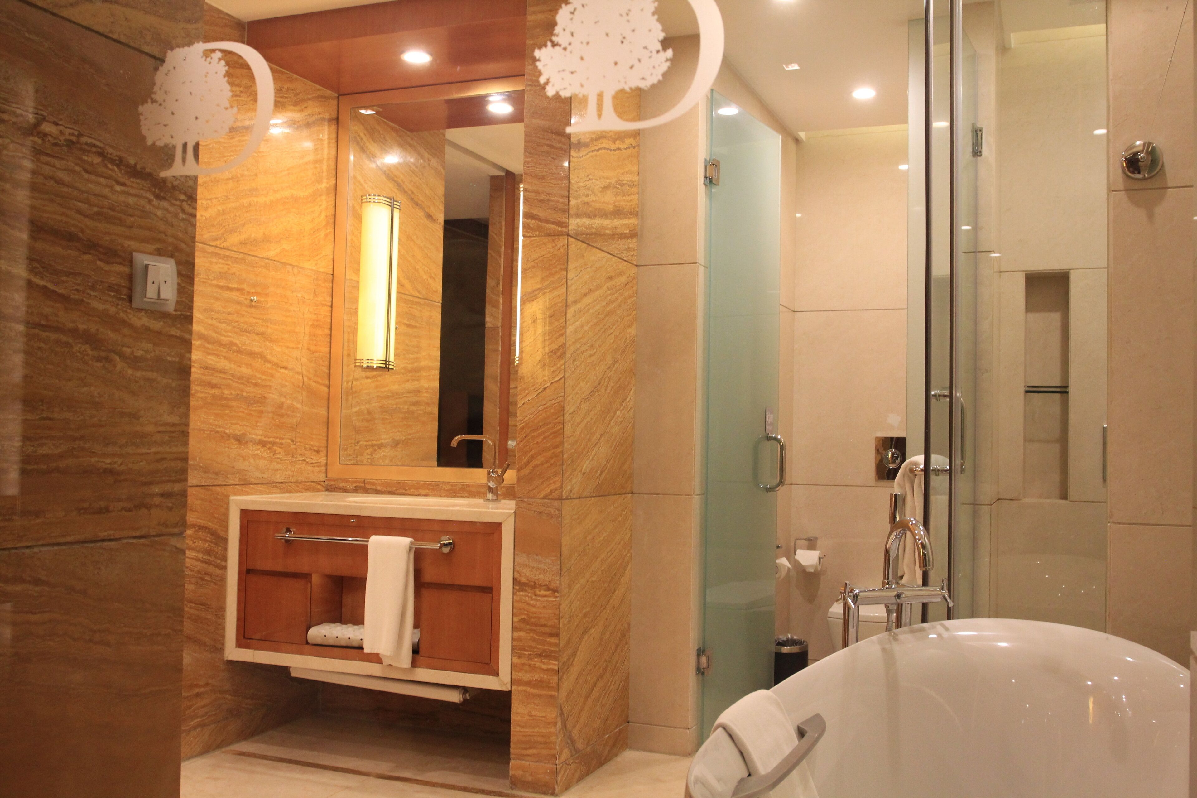 A modern bathroom with a marble vanity, a large mirror, a glass shower enclosure, and a bathtub.
