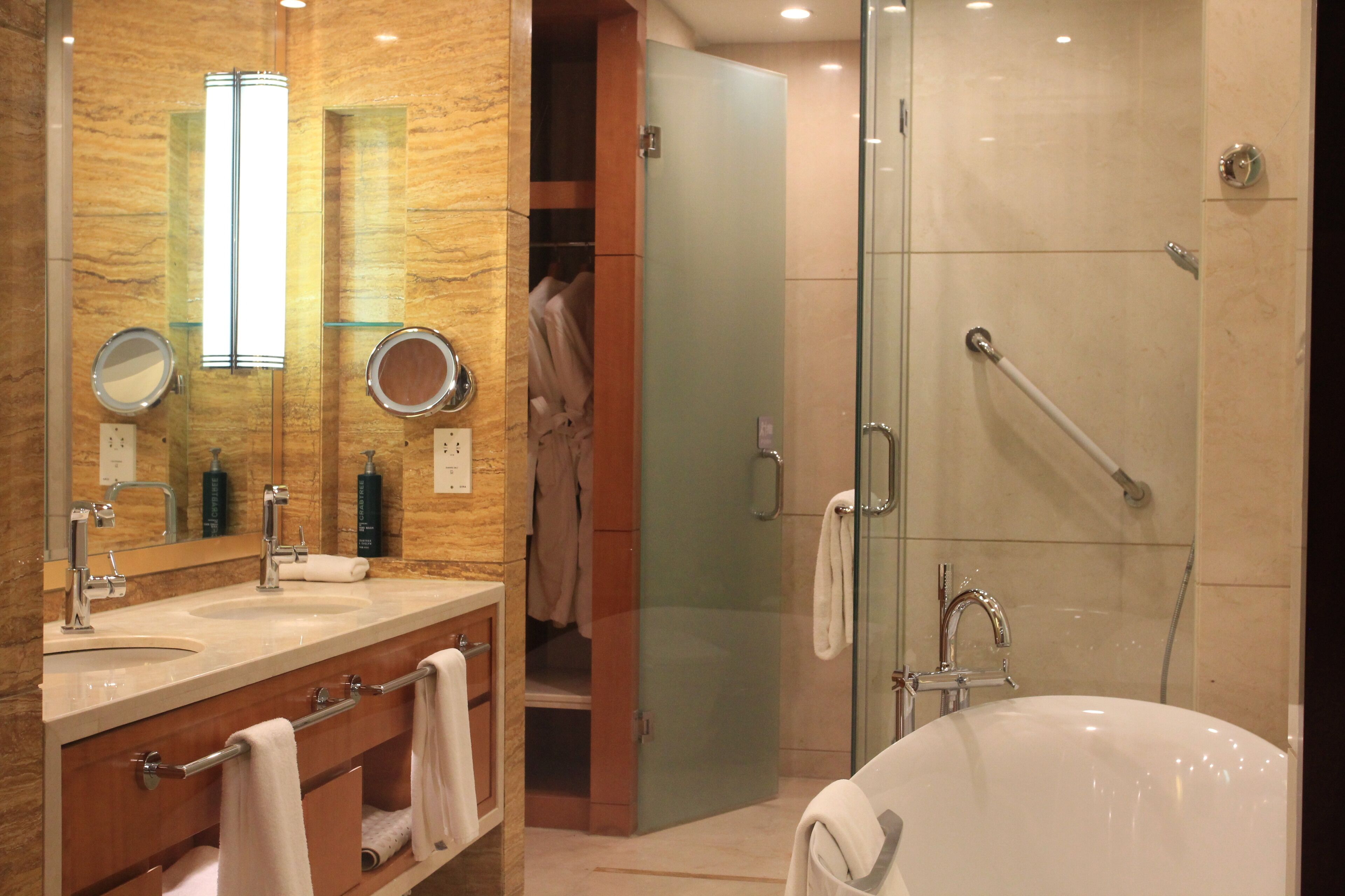 Un baño moderno con dos lavamanos, un espejo grande, ducha con mampara de vidrio y vestidor.