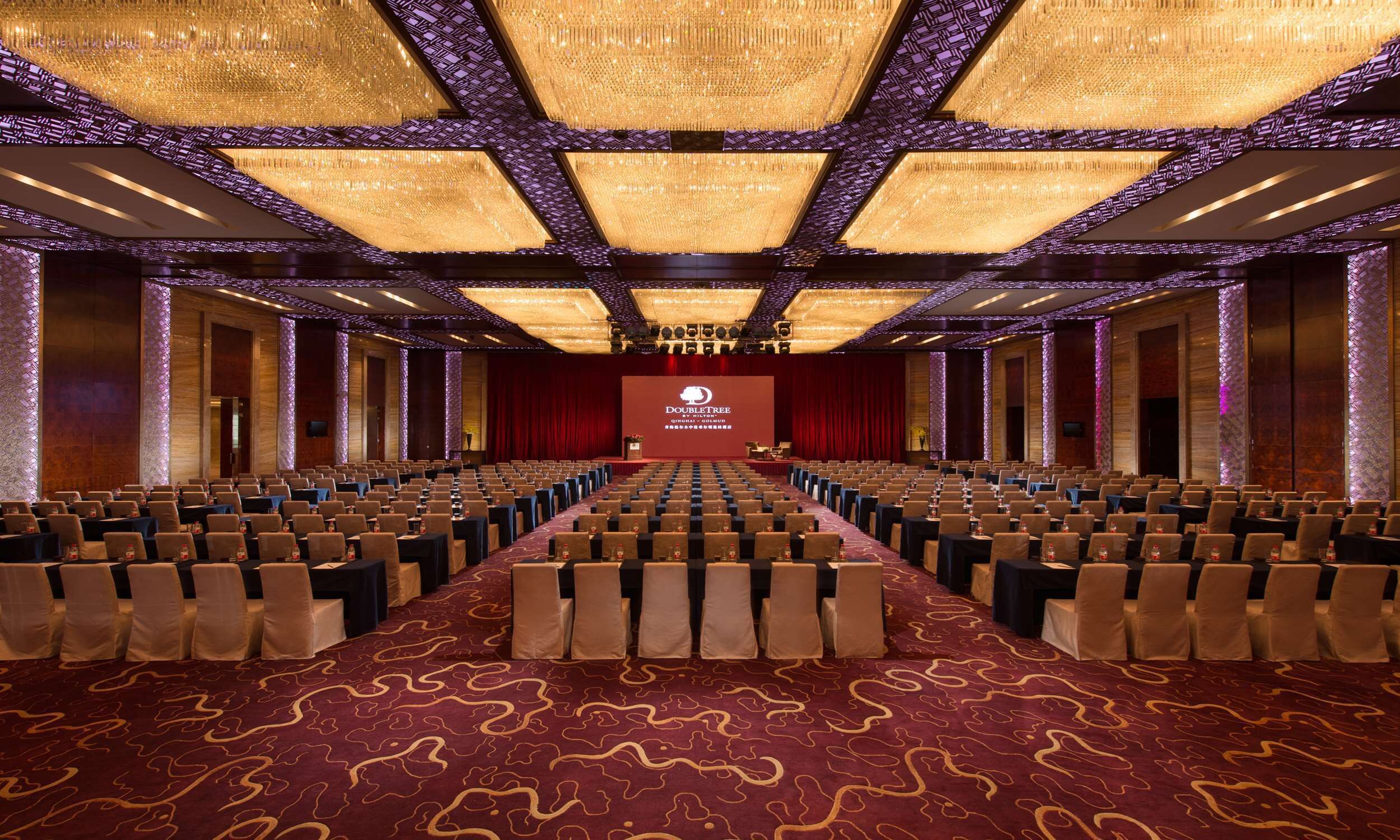 A large conference room with rows of chairs, a red carpet, and a stage with a podium.