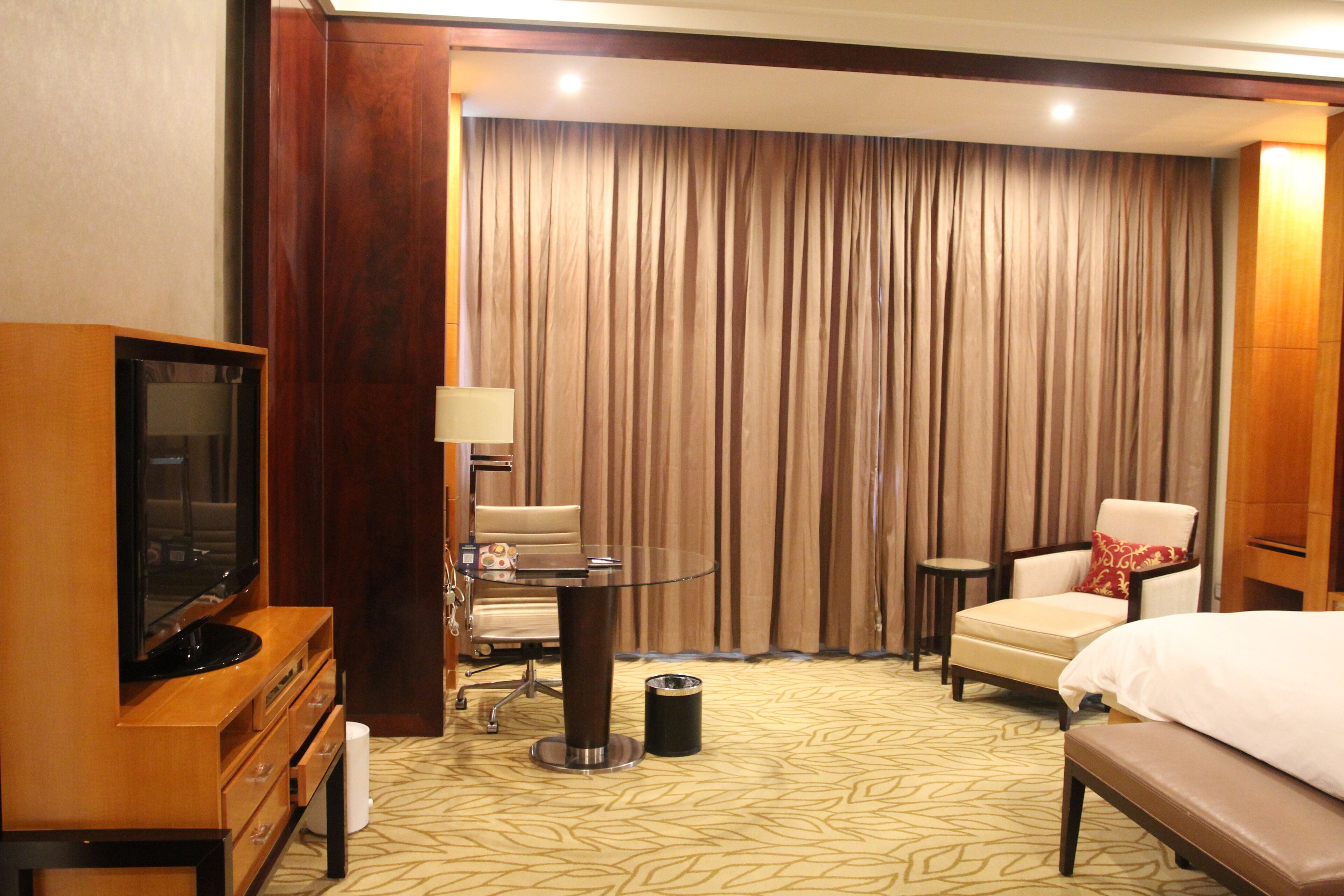 A hotel room with a bed, a TV, a desk, a chair, and a curtain.