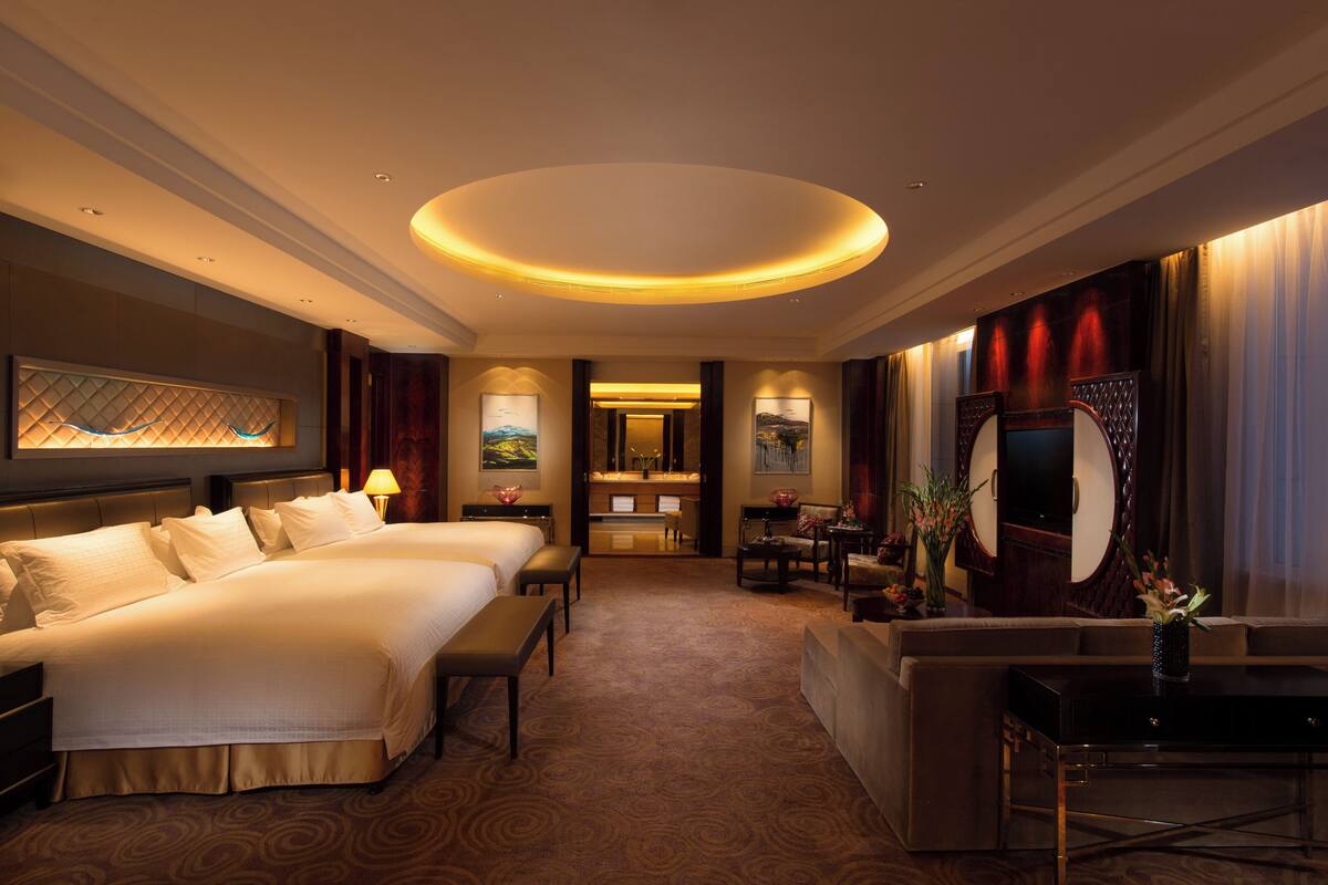 A hotel room with two beds, a desk, a vanity, and a large mirror.