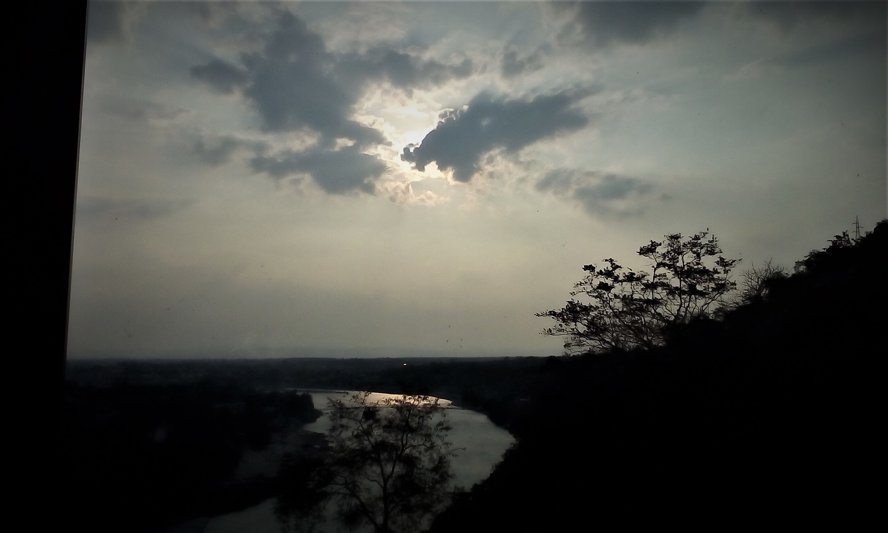 A river with a tree on the right and a cloudy sky.