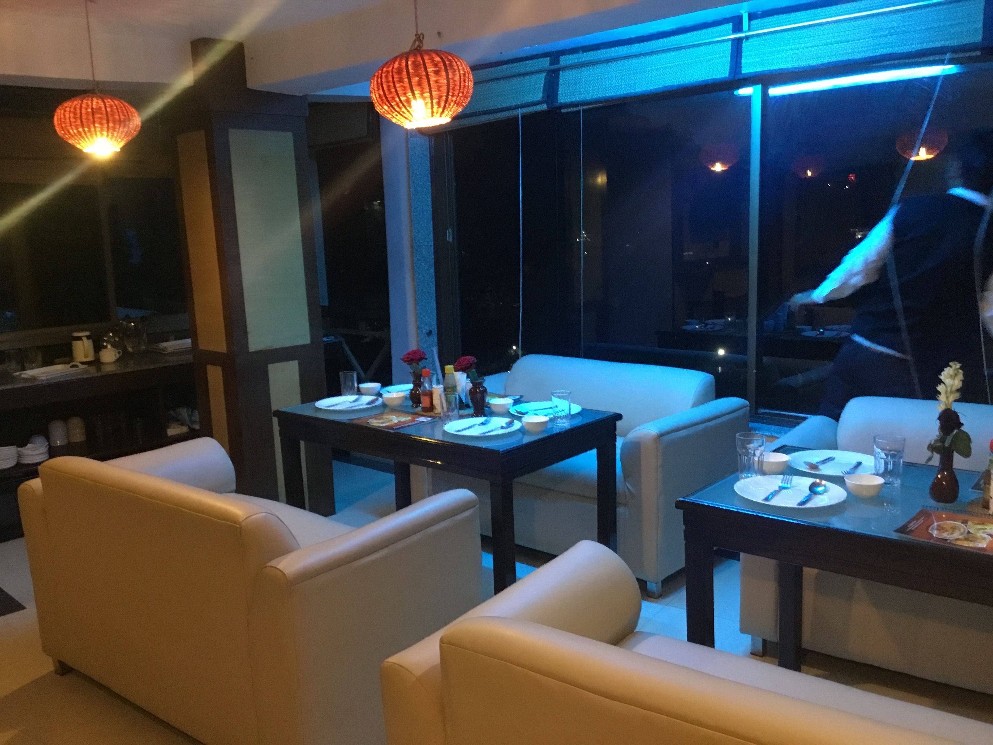 A modern dining area with a table set for two, a sofa, and a large window with a view of the city at night.