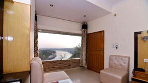 Quarto com vista para um rio, um sofá, uma mesinha de centro com controles remotos e um armário de madeira.