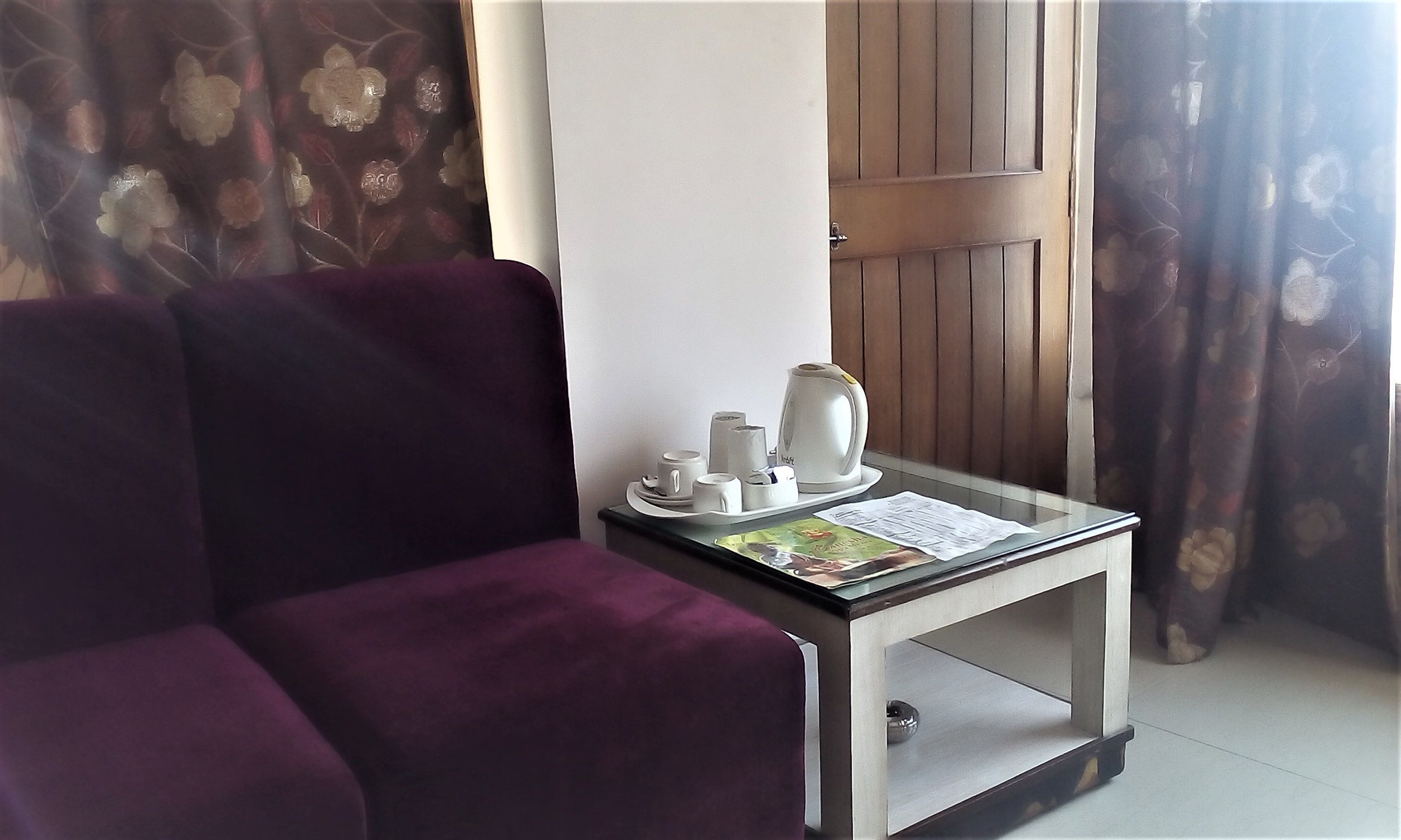 Habitació amb un sofà morat, una taula petita amb una paperera, tasses i una revista.