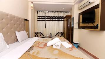 A hotel room with a large bed, a television mounted on the wall, a small table with chairs, and a window with curtains.