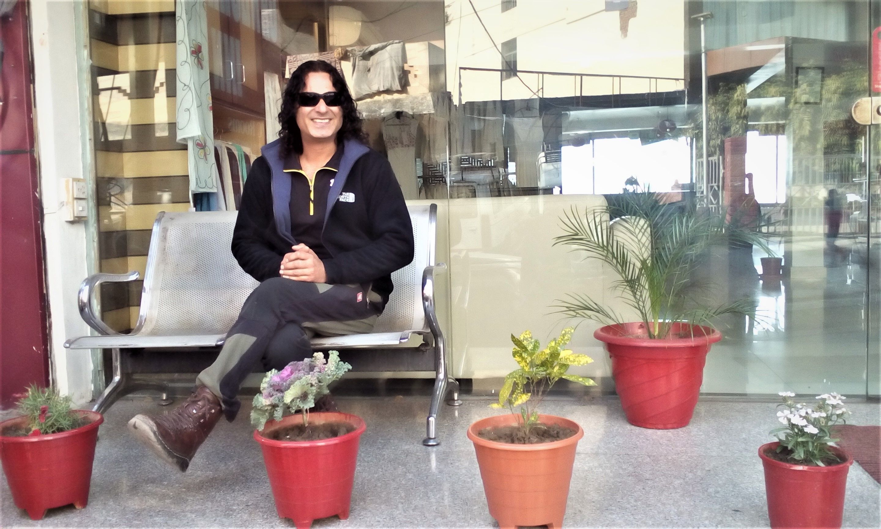 A person sitting on a bench outside a building with potted plants in front.