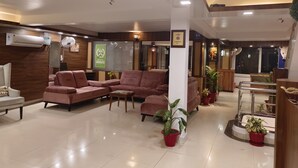 Um saguão de hotel com áreas de estar, um balcão de recepção e uma grande janela com persianas.