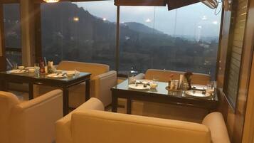 A restaurant with tables set for dining, large windows offering a view of the hills, and hanging lights.
