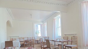 Un comedor amplio con varias mesas y sillas, ventanas grandes con cortinas y un techo de diseño clásico.