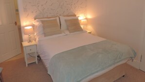 Una cama bien hecha con dos almohadas, una lámpara de noche y una mesita de noche.