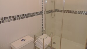 Ducha con cerramiento de vidrio, cabezal de ducha manual y grifo empotrado.