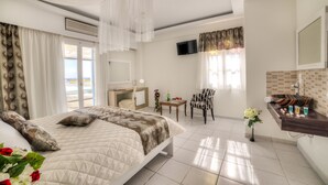 A hotel room with a bed, a desk, a chair, a TV, and a bathroom. - Pantheon Hotel (Santorini)