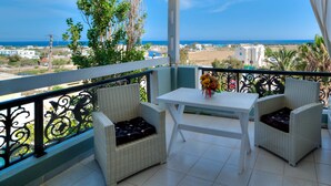 A balcony with wicker furniture, a table, and a vase of flowers. - Pantheon Hotel (Santorini)