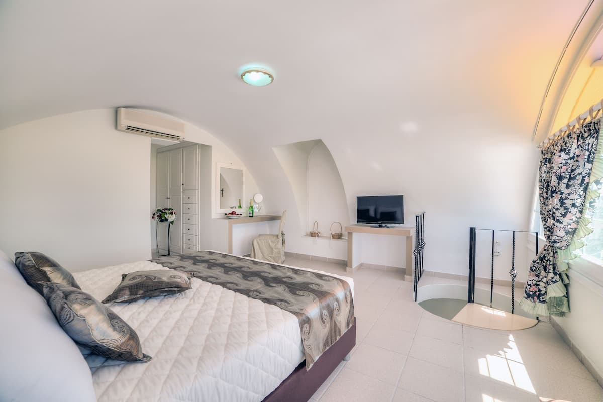 Ein Schlafzimmer mit Bett, Schreibtisch, Fernseher und einem Fenster mit Vorhängen.
