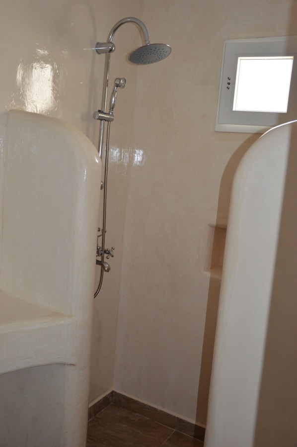 A bathroom with a shower, a toilet, and a wall-mounted light fixture. - Pantheon Hotel (Santorini)