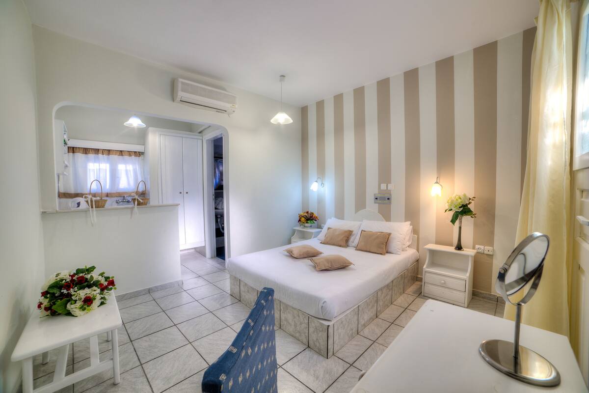 Ein Schlafzimmer mit einem Bett, Nachttisch, Spiegel und einem kleinen Tisch mit Blumen.