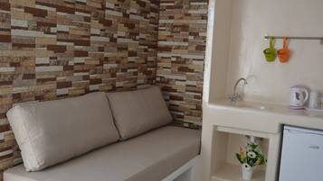 A room with a beige sofa against a wall with a mosaic tile pattern, a sink with a faucet, and a small refrigerator.