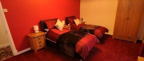 A bedroom with two beds, a wooden wardrobe, and a red carpet.