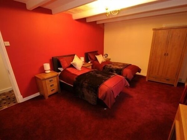 A bedroom with two beds, a wooden wardrobe, and a red carpet. - The Three Wheat Heads (Morpeth)