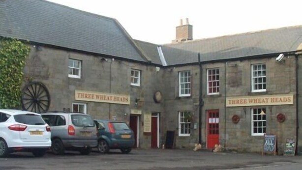 A building with a sign reading "Three Wheat Heads" and a large wheel visible outside.