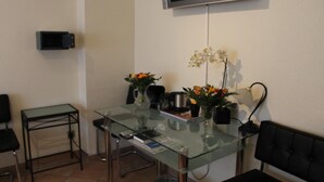 A small, modern room with a glass table, two chairs, a TV, and a few potted plants. - Hotel Müller (Cologne)