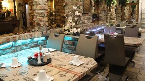 A restaurant with brick walls, a stone bench, and tables with patterned tablecloths. - Hotel Müller (Cologne)