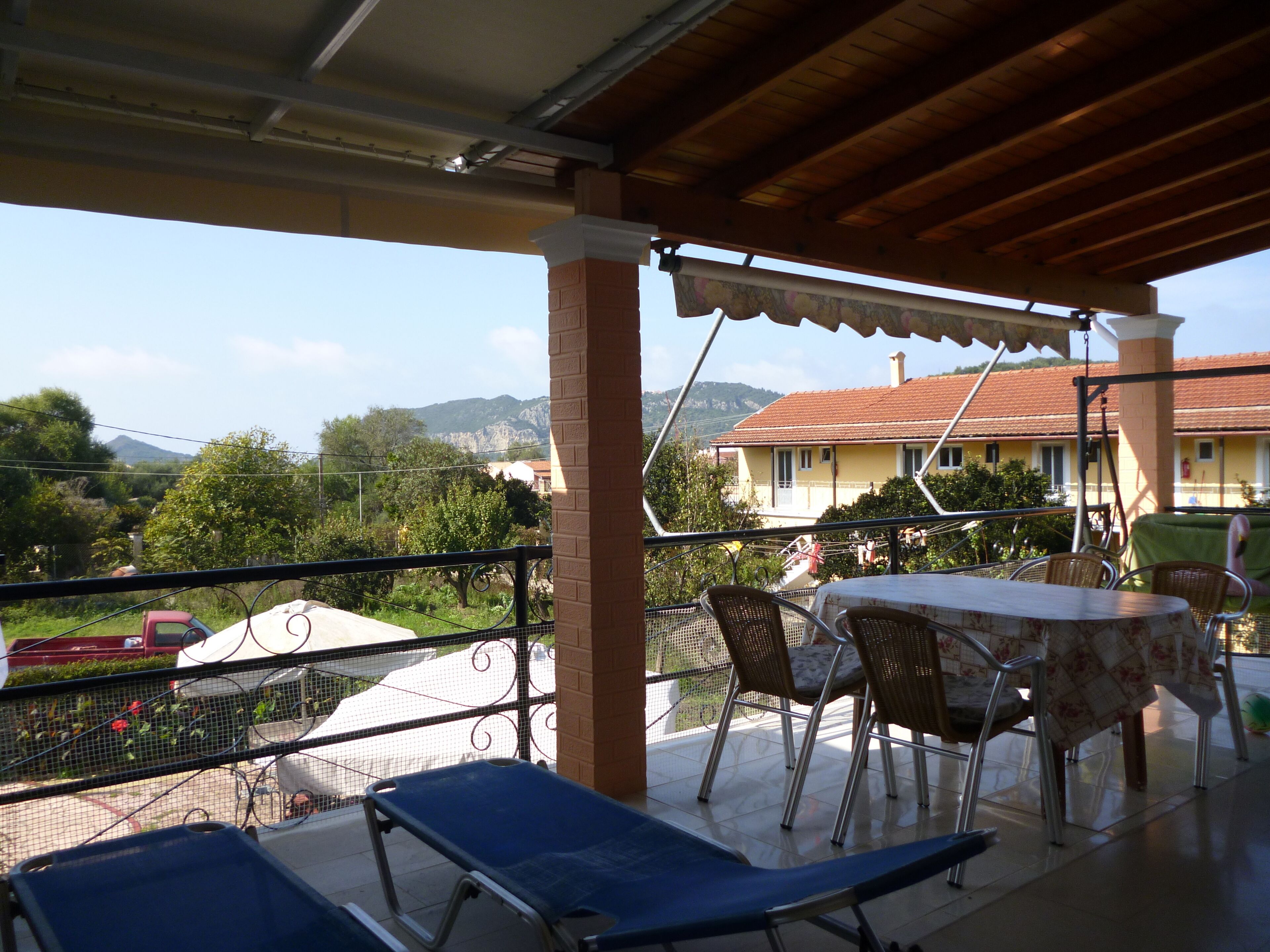 A covered outdoor area with a table and chairs, overlooking a mountainous landscape.