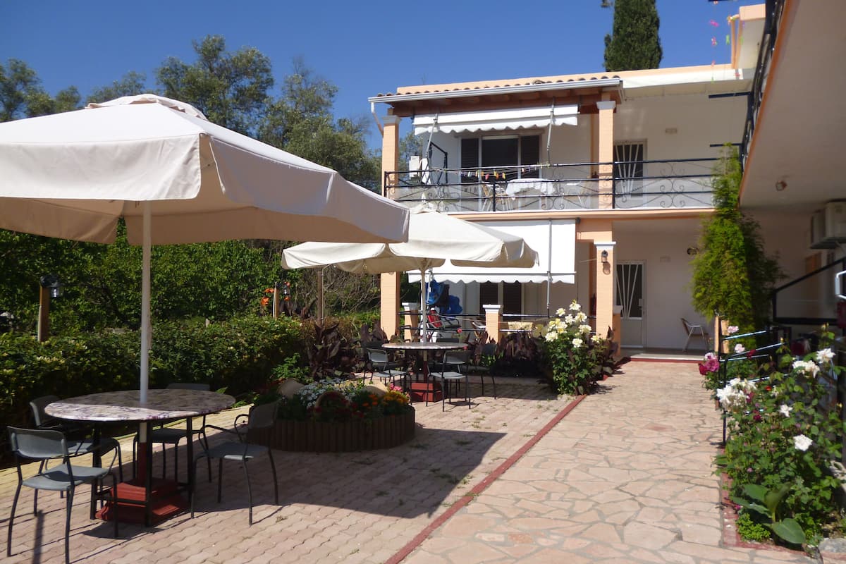 An outdoor patio area with tables and chairs, a covered seating area, and a building with a balcony.