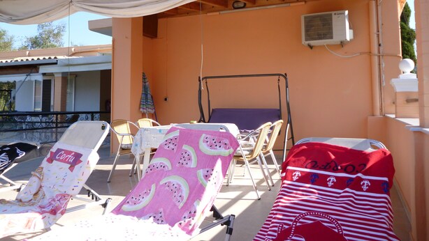 A covered outdoor seating area with lounge chairs, a table, and a ceiling with wooden beams and a white awning. - Kostas Apartments & Studios (Corfu)