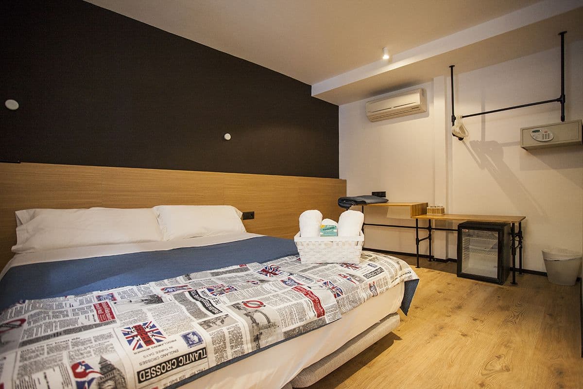 Quarto de hotel com cama grande, pequena escrivaninha e cozinha compacta.